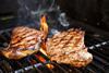 Beef steaks cooking in open flame on barbecue grill