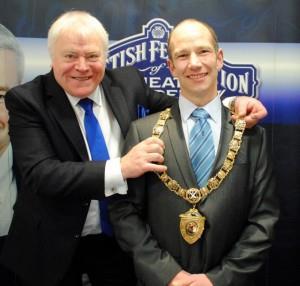 Past president Ian Faulds places the chain around the neck of new president Beaton Lindsay.