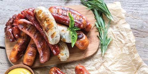 Cooked sausages on a wooden serving board, garnished with herbs.